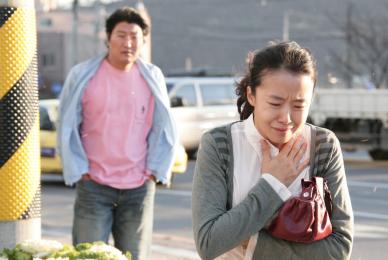 woman clutching chest and crying with man in pink shirt standing behind her looking